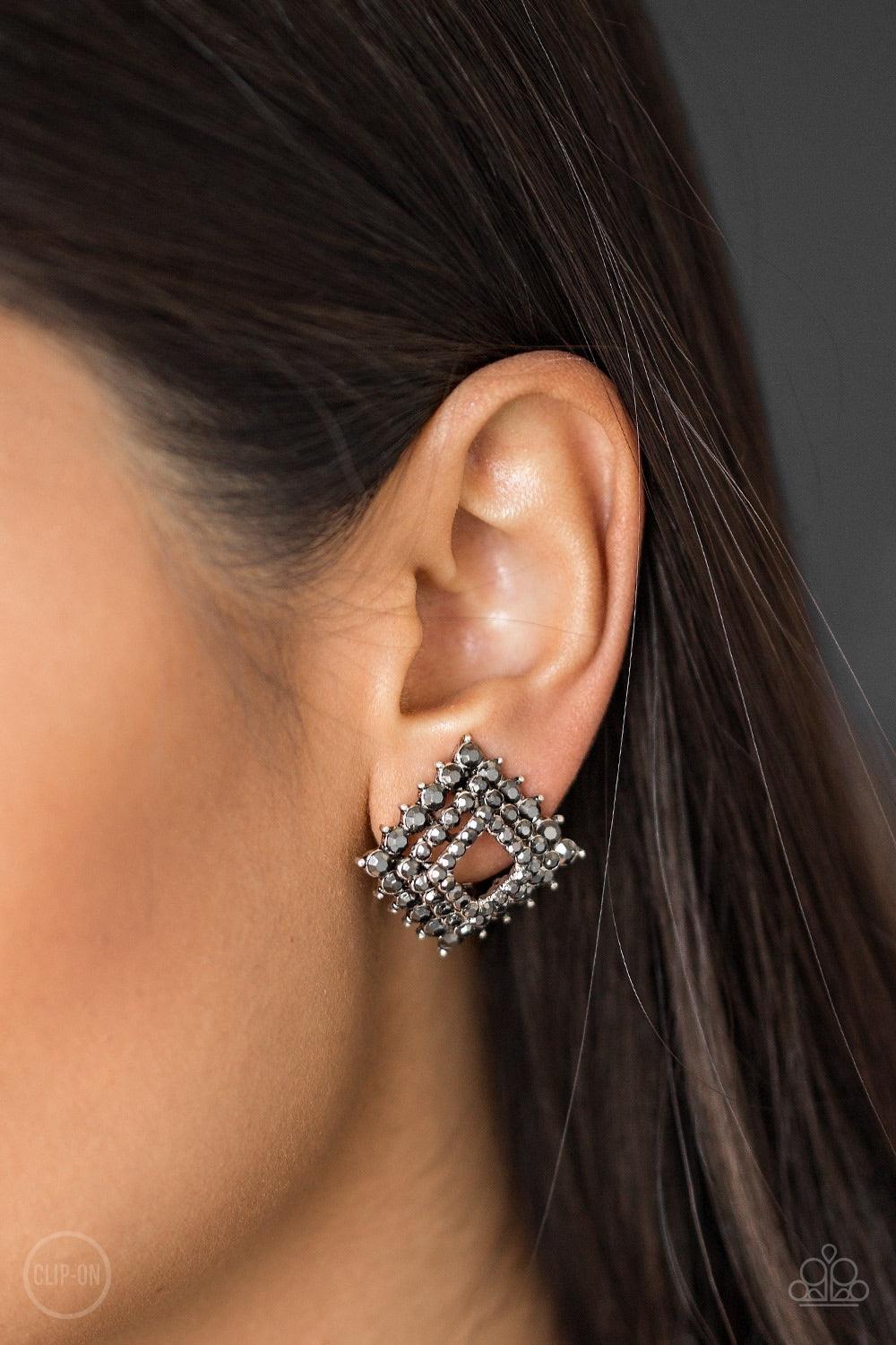 Paparazzi Accessories Kensington Keepsake - Silver *Clip-On Gradually increasing in size, glittery hematite rhinestones are encrusted along three stacking gunmetal frames for a regal look. The square frames slightly curve in towards the ear for an edgy fi