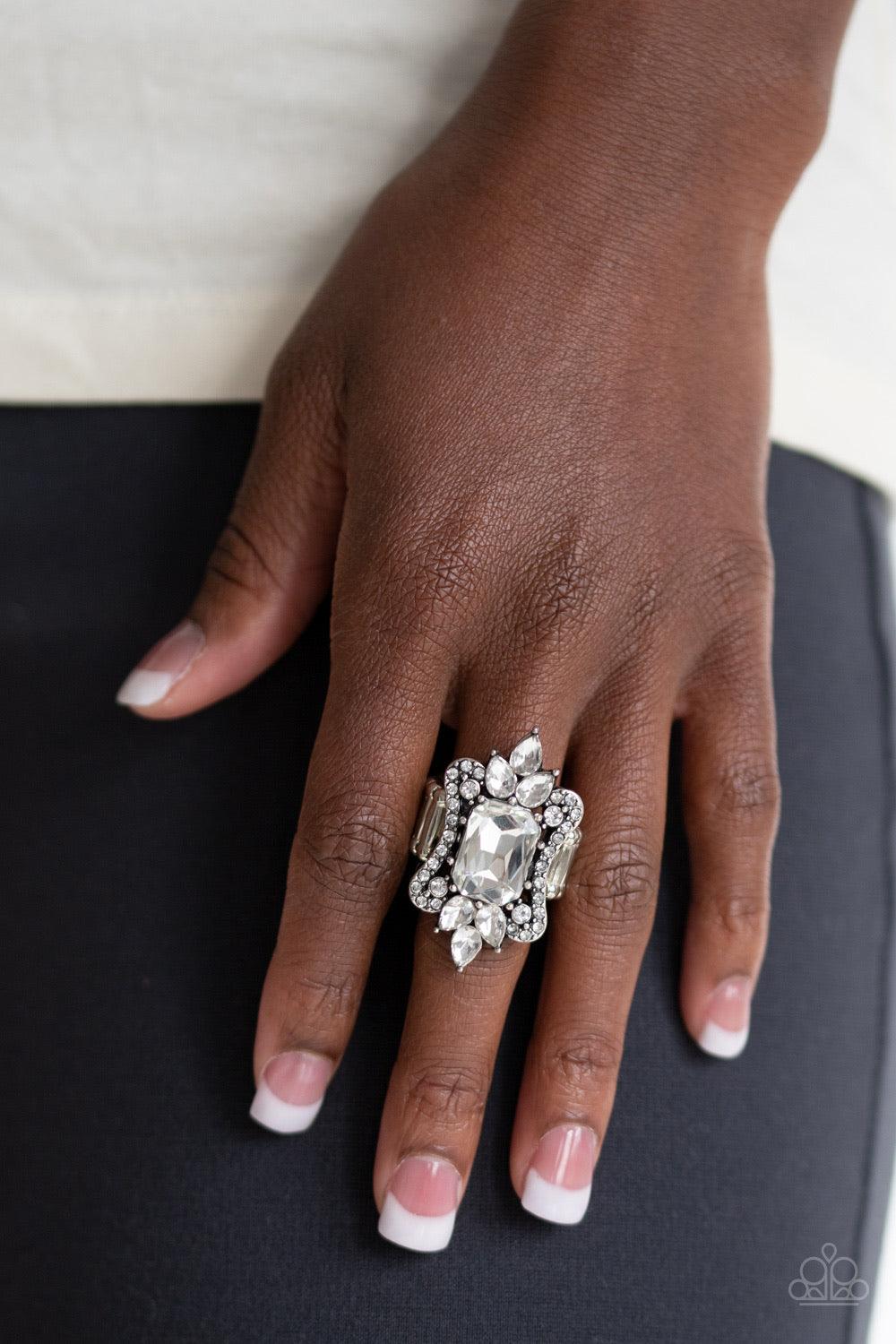 Paparazzi Accessories Things That Go Boom - White A blinding collection of round and teardrop white rhinestones coalesce around an oversized emerald-style gem, creating a dramatic statement piece atop the finger. Features a stretchy band for a flexible fi