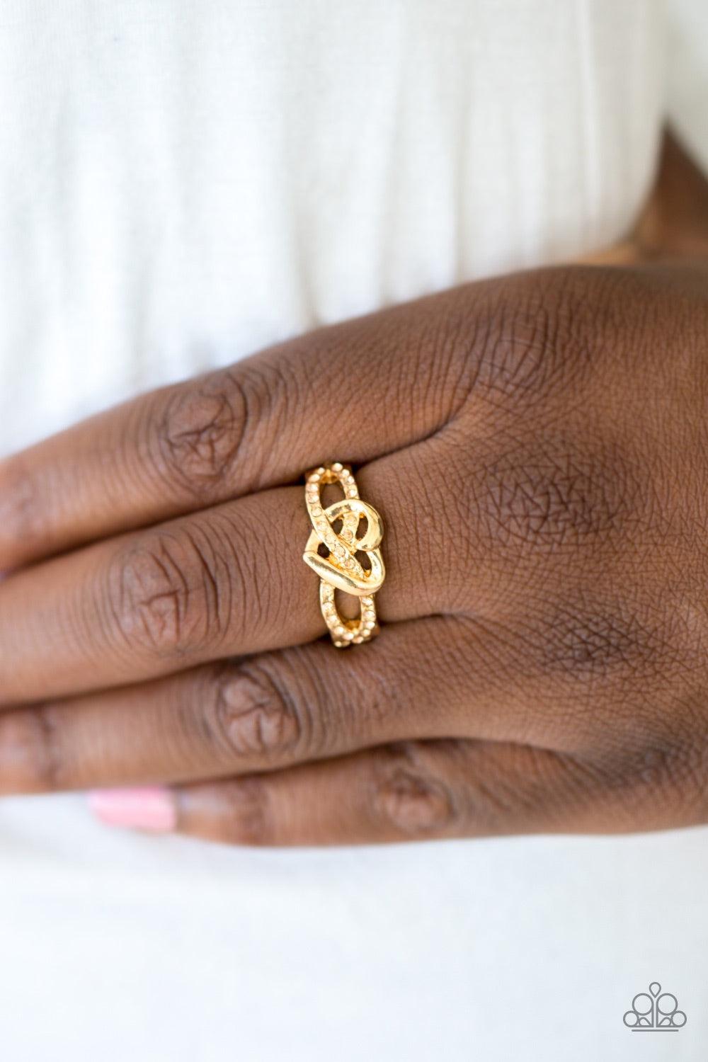 Paparazzi Accessories Heavenly Heart - Gold Encrusted in glittery peach rhinestones, golden ribbons crisscross across the finger, creating a dainty band. A glistening gold heart adorns the center of the band for a romantic finish. Features a dainty stretc