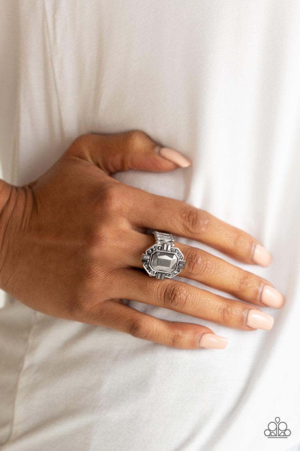 Paparazzi Accessories Outta My Way ~Silver Featuring a regal emerald-style cut, a faceted hematite gem is pressed into the center of a silver frame radiating with smoky hematite rhinestones. Features a stretchy band for a flexible fit.
