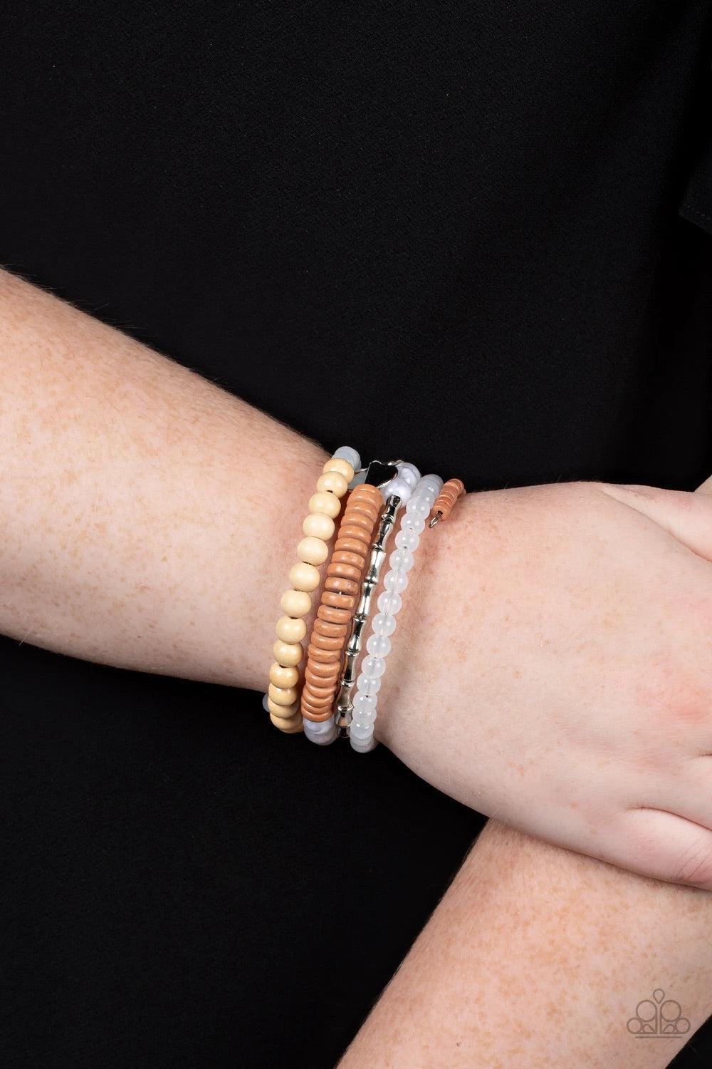Paparazzi Accessories Free-Spirited Spiral - White Mismatched sections of glassy and opaque white beads join silver discs, brown wooden beads, and brown disc-like beads along a coiled wire, creating an earthy infinity wrap bracelet around the wrist. Sold