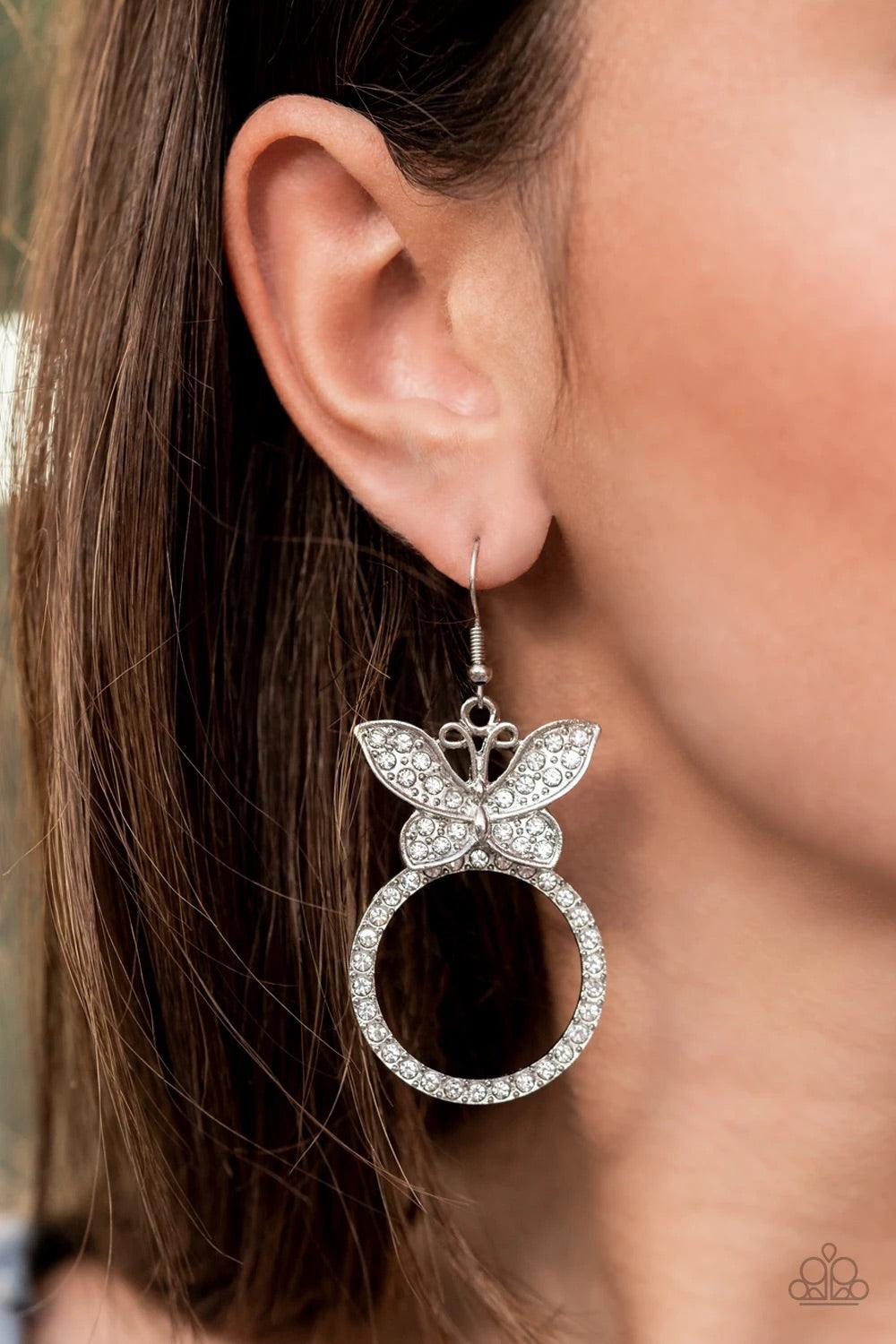 Paparazzi Accessories Paradise Found - White A white rhinestone encrusted silver butterfly flutters atop a silver ring dotted in matching white rhinestones, resulting in a dazzling statement piece. Earring attaches to a standard fishhook fitting. Sold as