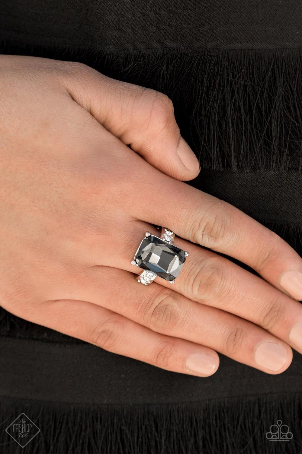 Paparazzi Accessories Bring Down the POWERHOUSE - Silver Featuring an elegant emerald-style cut, an oversized smoky gem is pressed into the center of a dainty silver band dotted in glassy white rhinestones, resulting in some serious show-stopping sparkle.