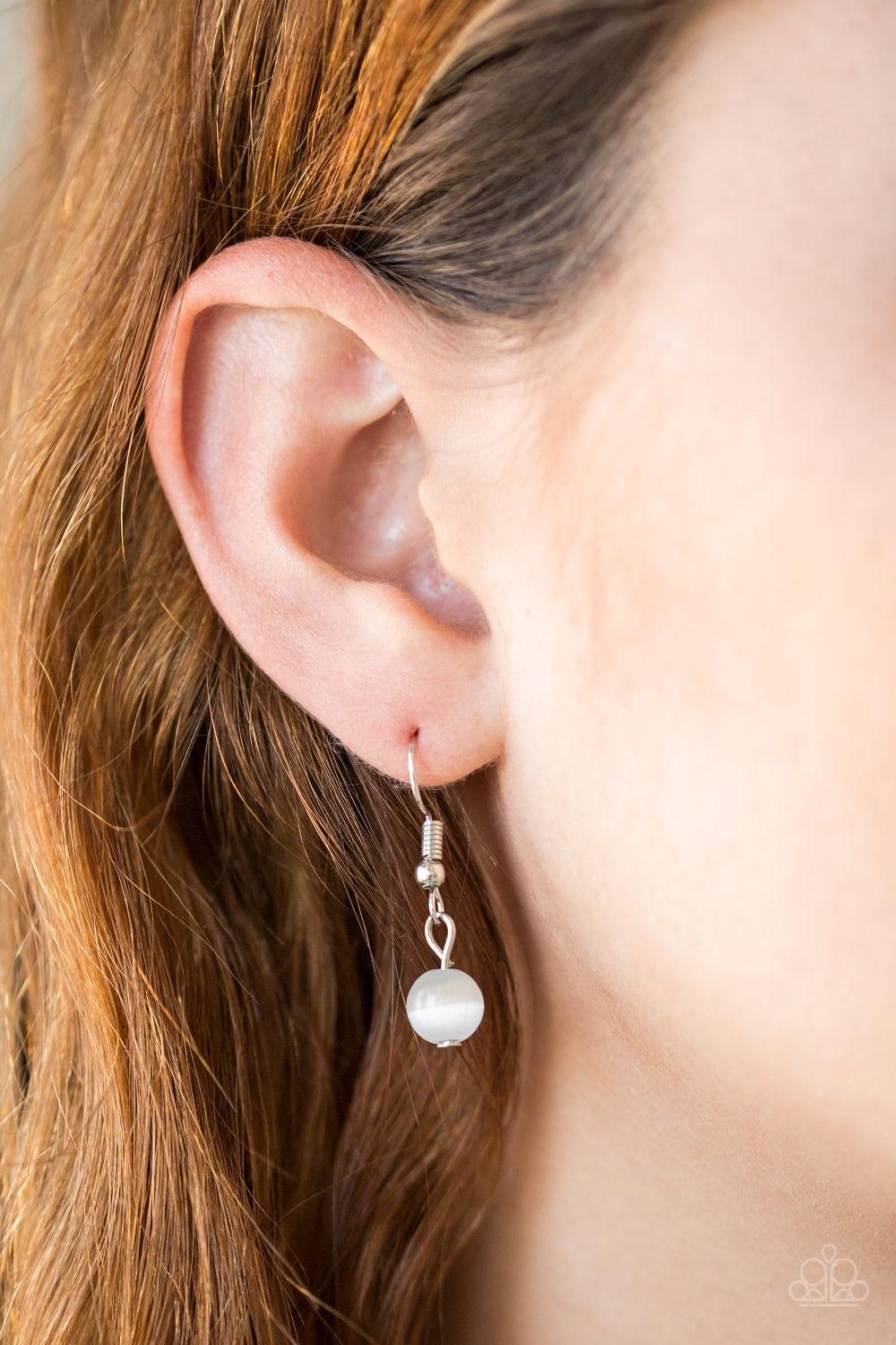 Paparazzi Accessories Nightcap And Gown - White Sporadically dotted in glittery white rhinestones, dainty silver circles join around the top of a glassy white teardrop moonstone. The bubbly pendant swings from the bottom of a lengthened silver chain for a