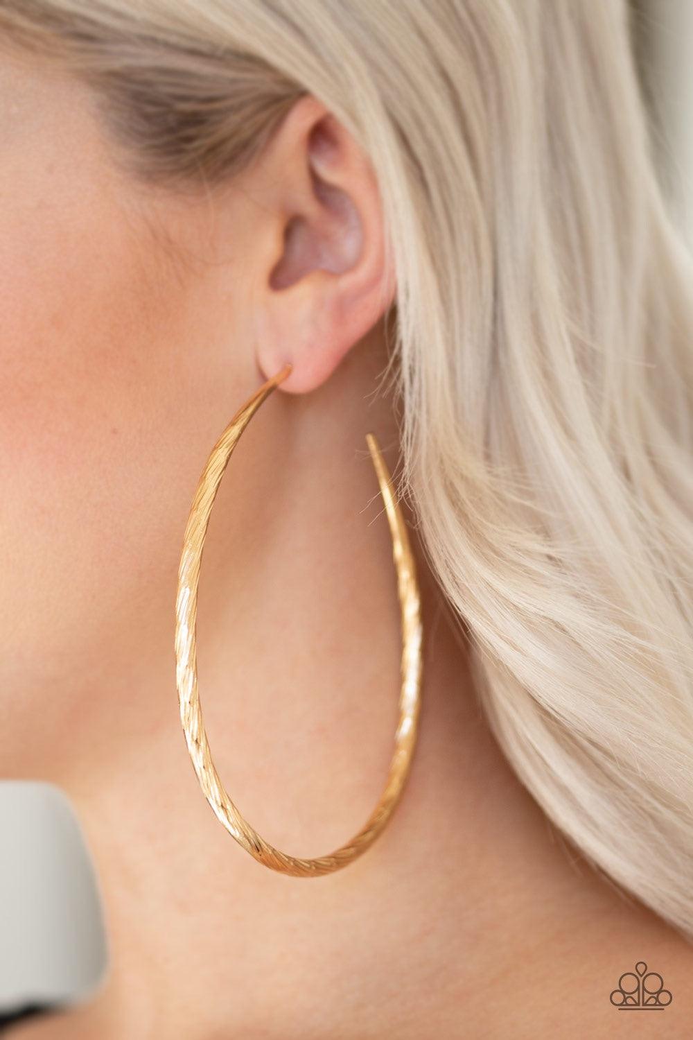 Paparazzi Accessories Fleek All Week - Gold Etched in shimmer, a rippling gold bar bends into a dramatic asymmetrical hoop for a showstopping look. Earring attaches to a standard post fitting. Hoop measures 3" in diameter. Jewelry