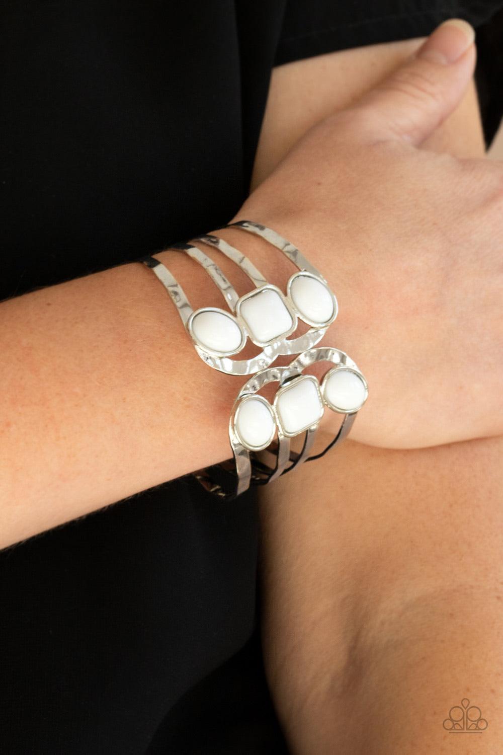 Paparazzi Accessories Mystified - White Dotted with oval and square white beads, hammered silver bars asymmetrically connect into two scalloped silver frames around the wrist, creating an adjustable open-faced cuff. Features a hinged closure. Sold as one