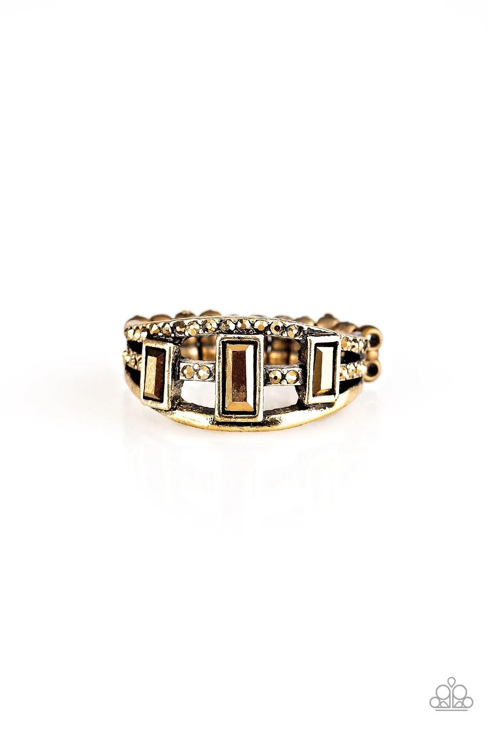 Paparazzi Accessories Noble Nova - Brass Three aurum emerald-cut rhinestones are encrusted along three brass bands radiating with smooth surfaces and sections of glittery aurum rhinestones for an edgy fashion. Features a stretchy band for a flexible fit.