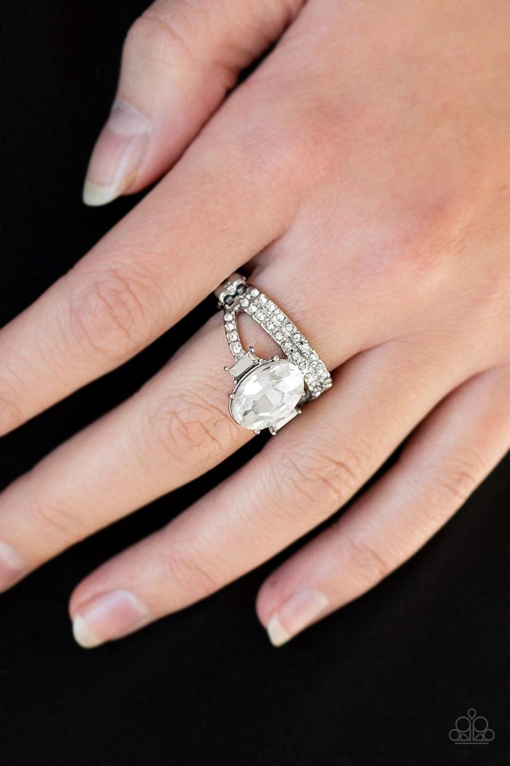 Paparazzi Accessories Bling Queen - White Encrusted in glassy white rhinestones, shiny silver bands arc across the finger. Infused with emerald style rhinestones, an over sized white rhinestone crowns the layered bands for a regal finish. Features a daint