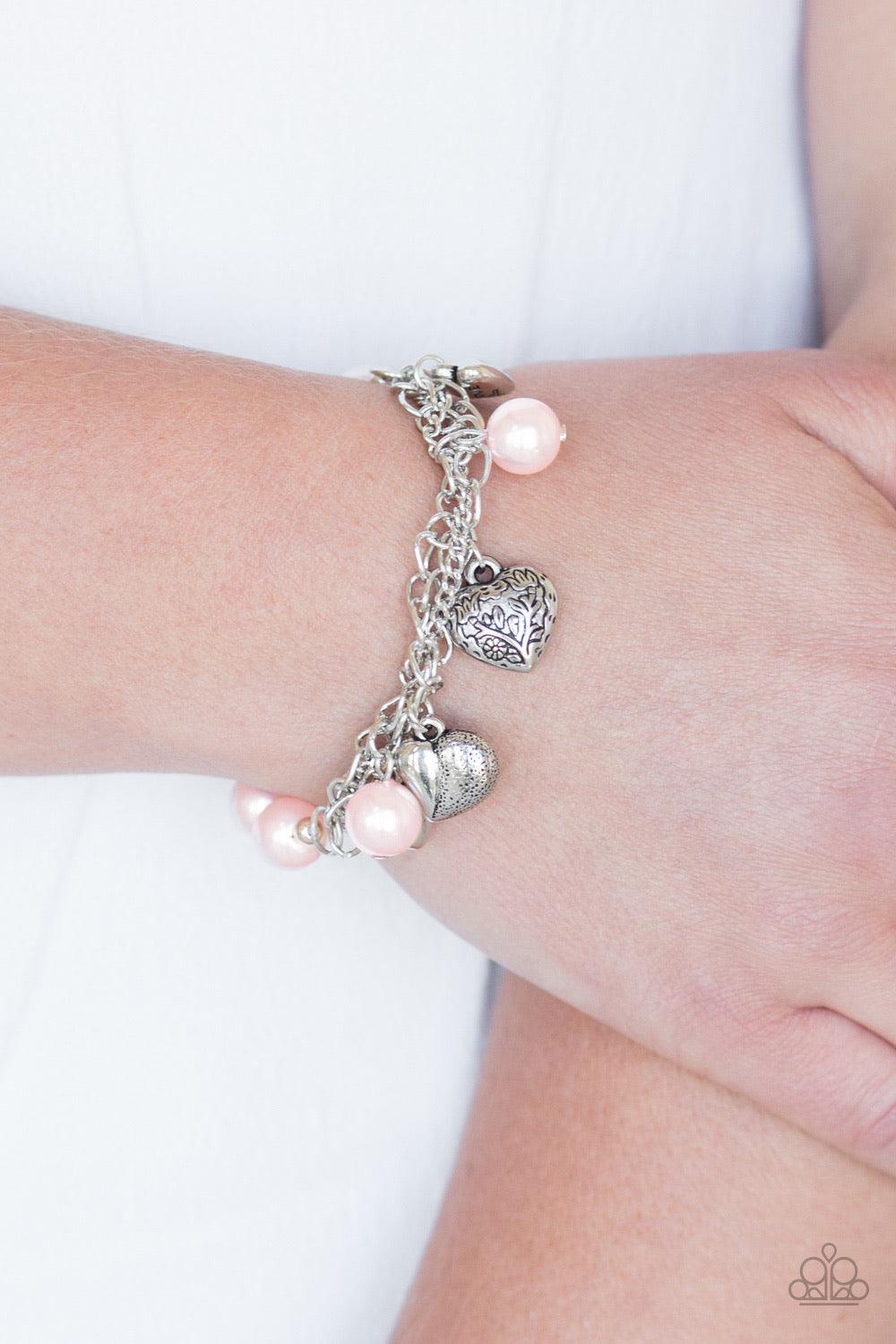 Paparazzi Accessories More Amour - Pink Attached to a section of shimmery silver chain, pearly pink and dainty silver beads are threaded along a stretchy band. Mismatched silver heart charms swing from the glistening chain, creating a flirty fringe. Jewel