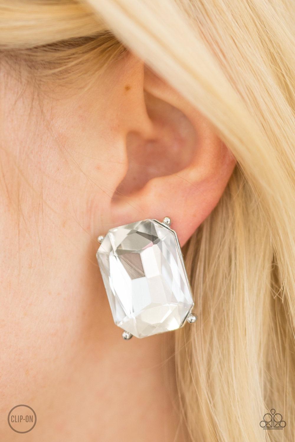 Paparazzi Accessories Opera House Hustle - White *Clip-On Featuring a regal emerald style cut, a glassy gem is pressed into a classic silver frame for a dramatic look. Earring attaches to a standard clip-on fitting. Jewelry