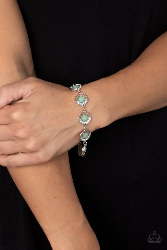 Paparazzi Accessories Twinkling Trajectory - Green An arc of glassy white rhinestones curls around one side of an opaque Basil gem inside a dainty silver hoop. The twinkly frames delicately link around the wrist, creating a mystical centerpiece. Features