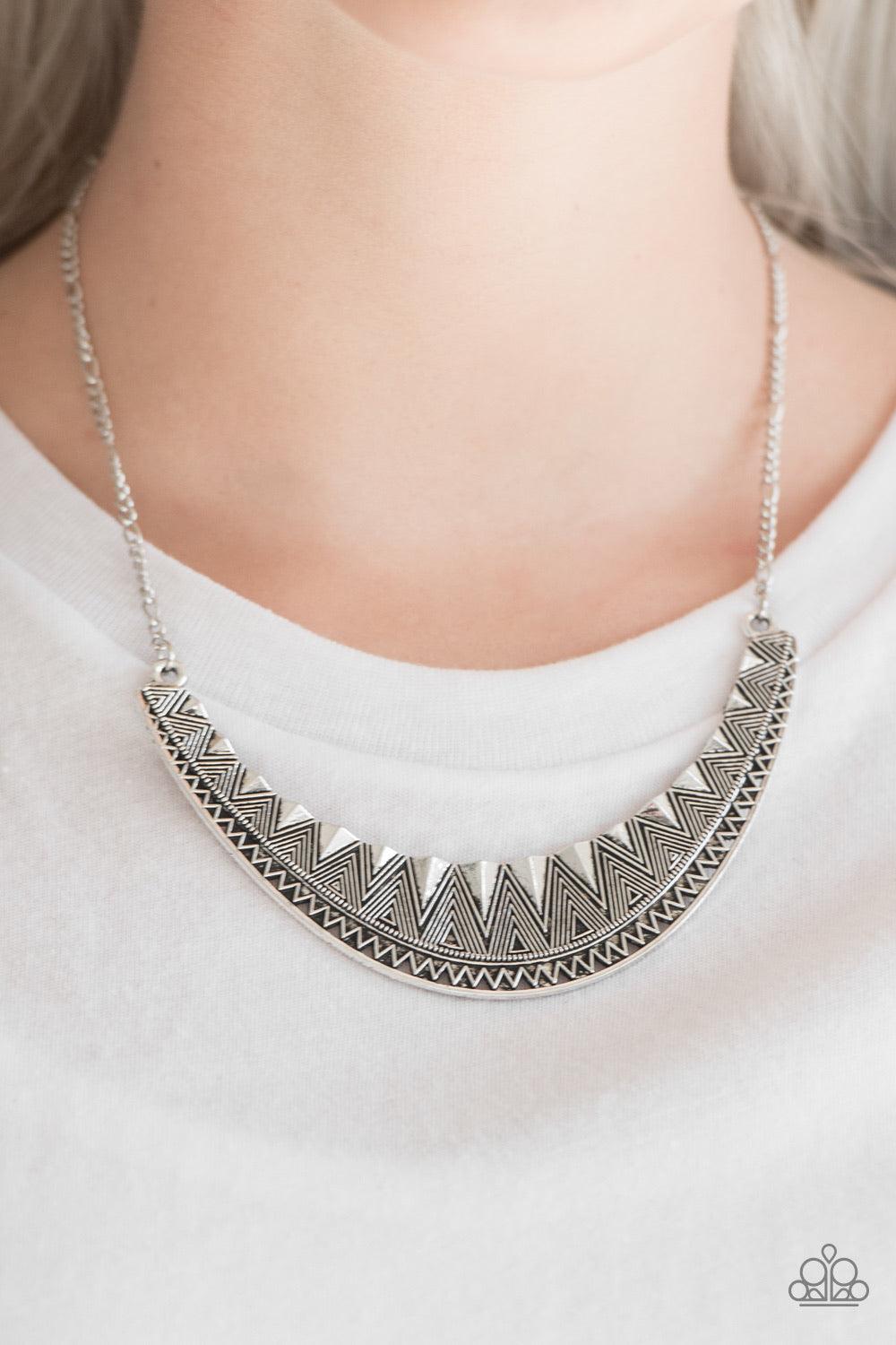 Paparazzi Accessories Thrown to The Lions - Silver Decorated in shimmery geometric detail, a glistening silver crescent swings below the collar, creating a bold tribal pendant. Features an adjustable clasp closure. Sold as one individual necklace. Include
