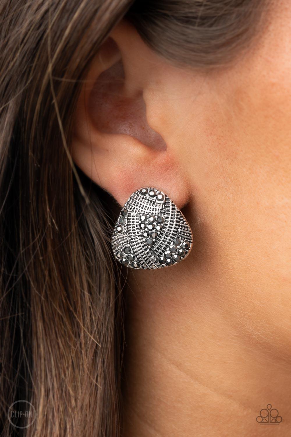 Paparazzi Accessories Gorgeously Galleria - Silver *Clip-On Studded and textured ribbons of silver wrap around sections of smoky hematite rhinestones, creating an edgy display. Earring attaches to a standard clip-on fitting. Sold as one pair of clip-on ea