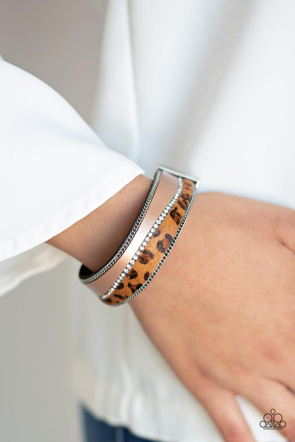 Paparazzi Accessories Flirtatiously Feline - Brown Infused with strands of antiqued silver chains and glassy white rhinestones, wavy pieces of tan leather and cheetah print line the front of a black suede band for a fierce look. Features an adjustable cla