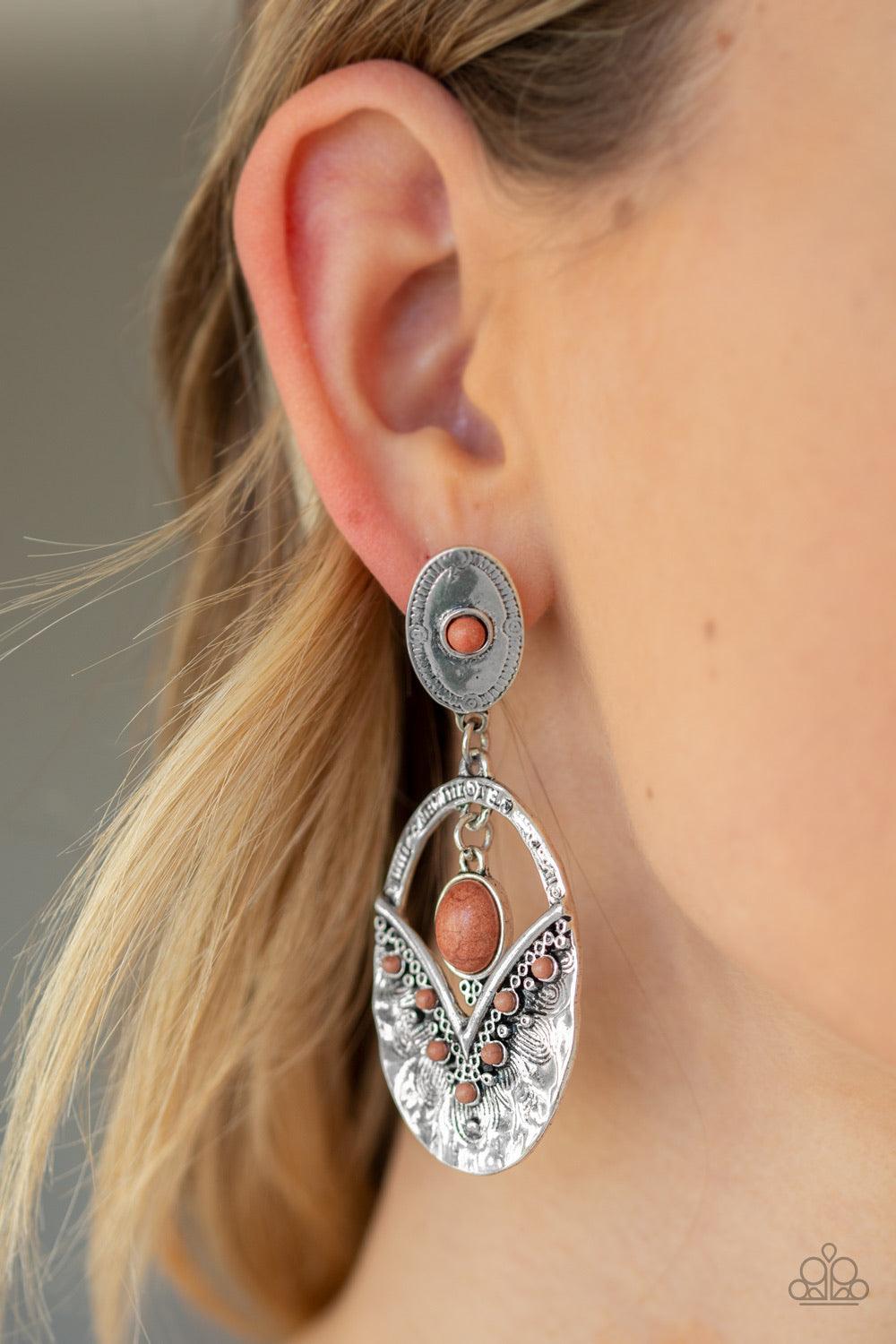 Paparazzi Accessories Terra Tribute - Brown Rippling with hammered silver textures, a brown stone dotted frame swings from the bottom of an ornate oval frame dotted with a matching brown stone. A smooth brown stone swings from the top of the ornate frame,