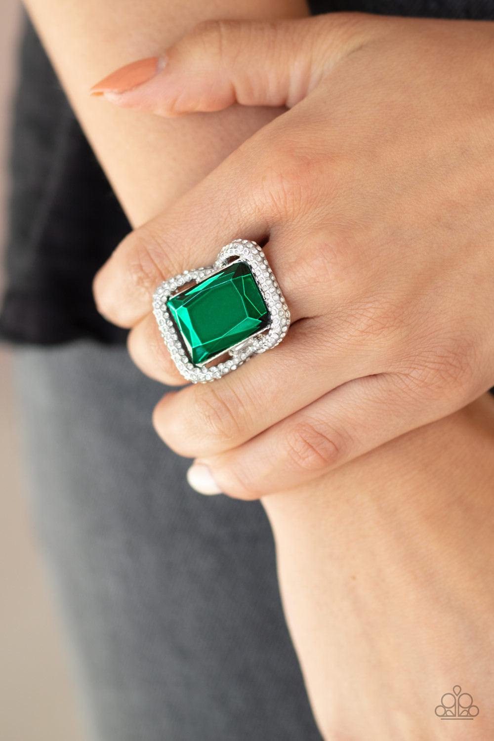 Paparazzi Accessories Deluxe Decadence - Green Featuring a regal emerald style cut, an oversized green gem nestles inside a rounded square silver frame encrusted in glassy white rhinestones for a dramatically glamorous look. Features a stretchy band for a