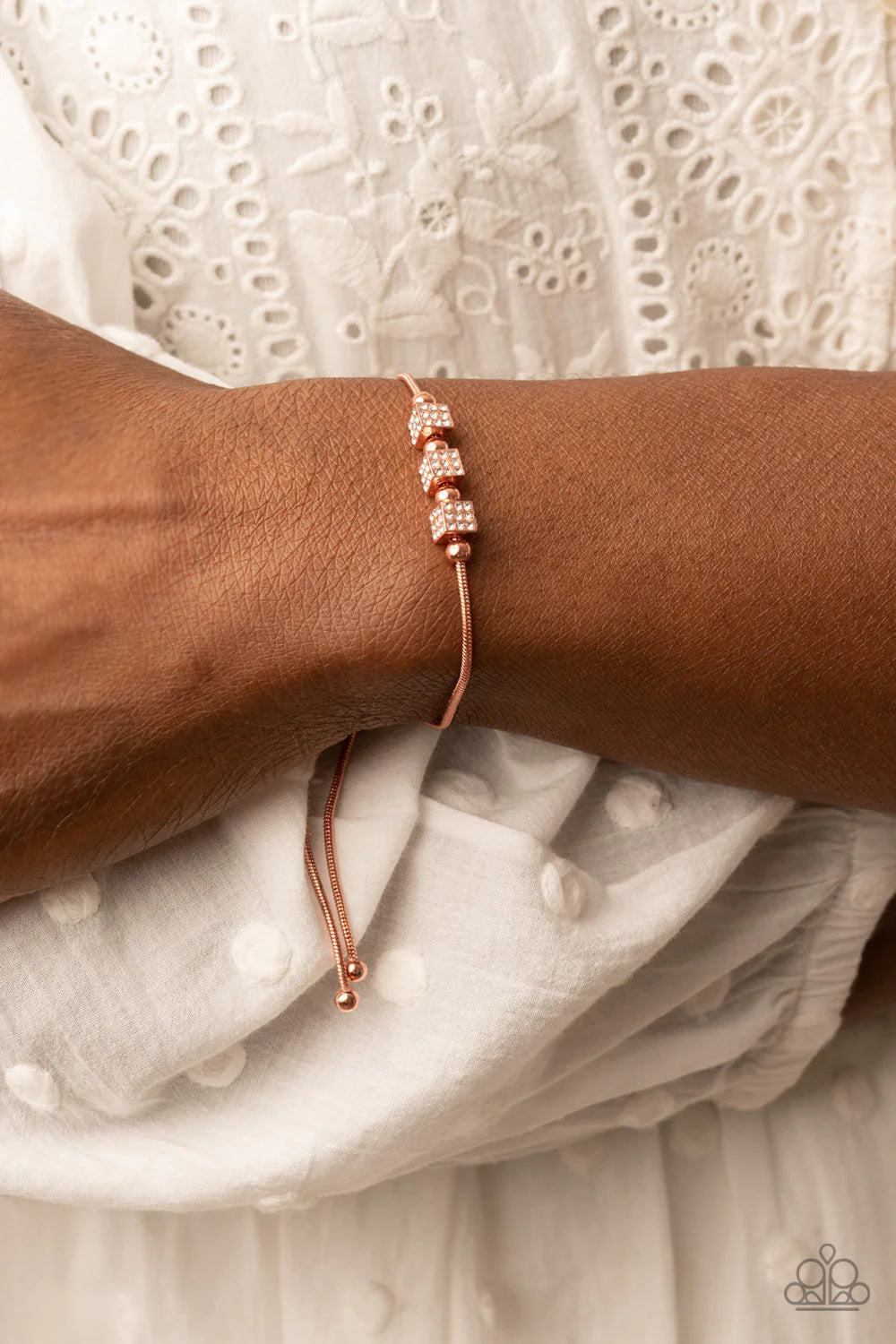 Paparazzi Accessories Roll Out the Radiance - Copper Dainty shiny copper beads and white rhinestone encrusted shiny copper cubes slide along a rounded shiny copper snake chain around the wrist, resulting in a radiant centerpiece. Features an adjustable sl