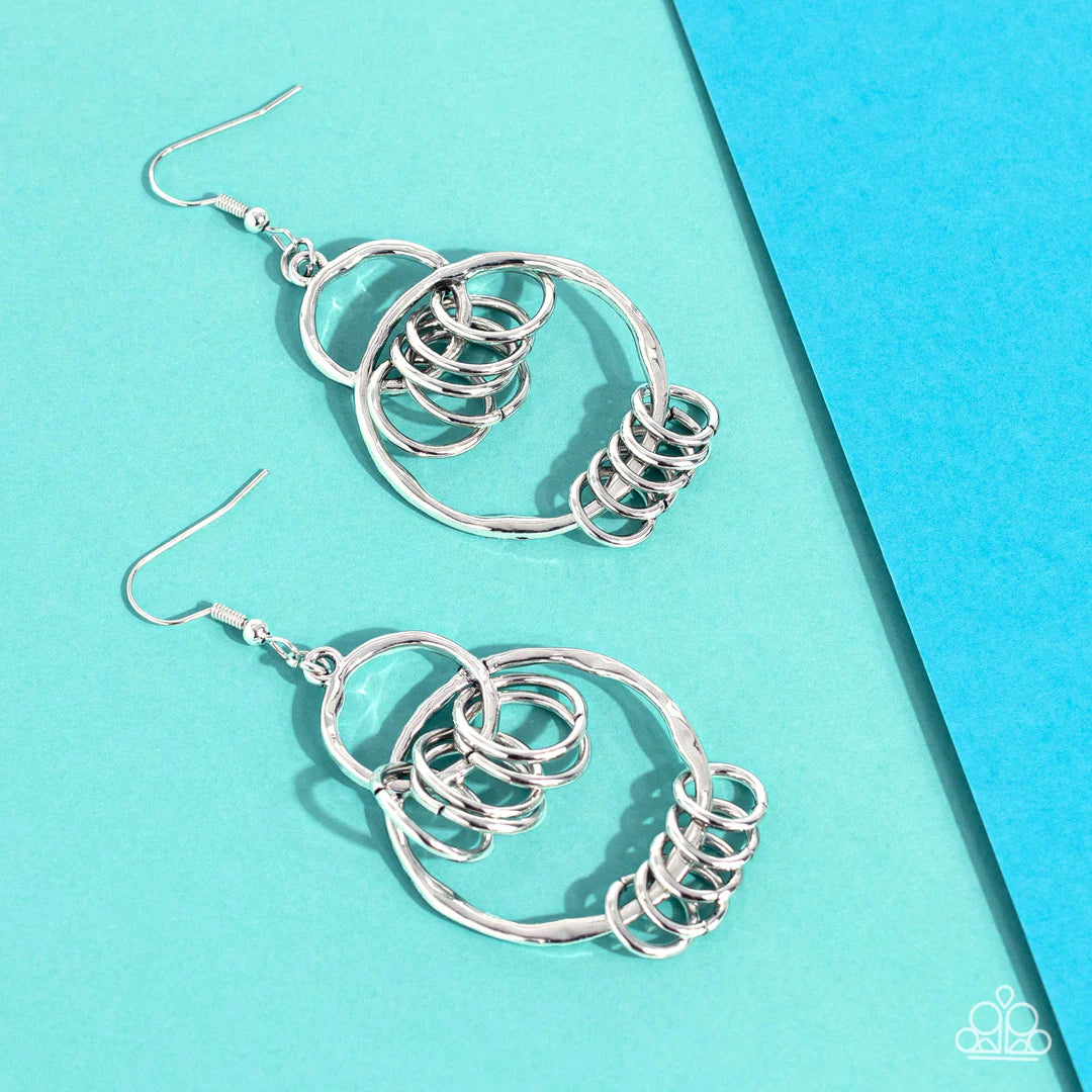 Paparazzi Accessories Rebel Ringer - Silver An antiqued collection of dainty silver rings swings from the bottoms of hammered silver hoops that interconnect into an edgy lure. Earring attaches to a standard fishhook fitting. Sold as one pair of earrings.