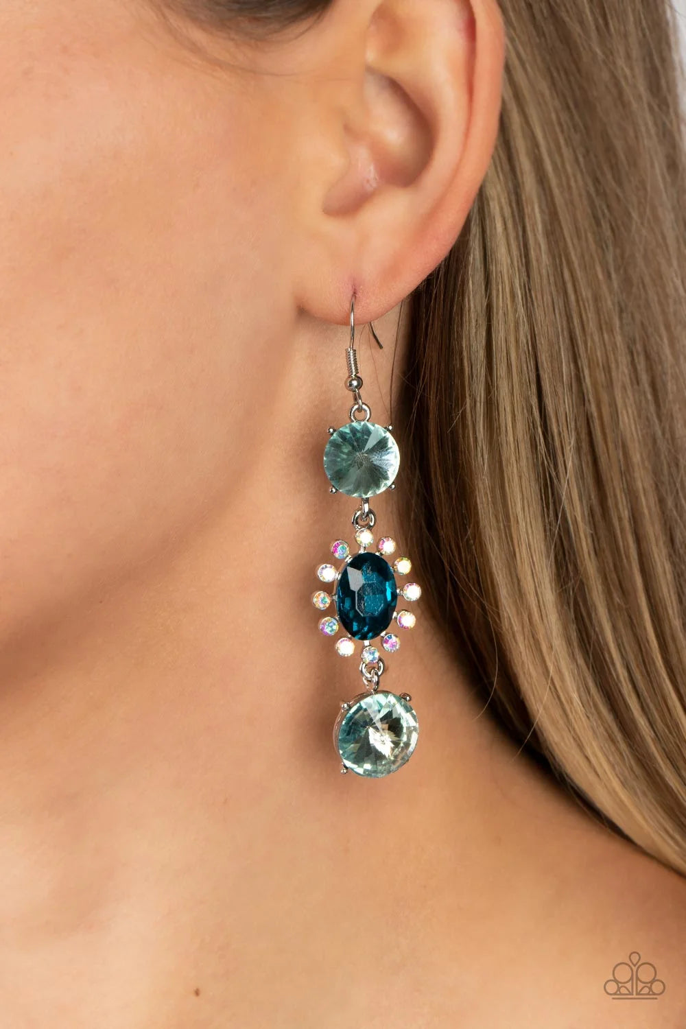 Paparazzi Accessories Magical Melodrama - Blue A trio of colorfully iridescent and brilliantly sparkling blue gems are linked together as they fall glamorously from the ear. A round-cut gem with an exaggerated faceted surface anchors the cascade, followed