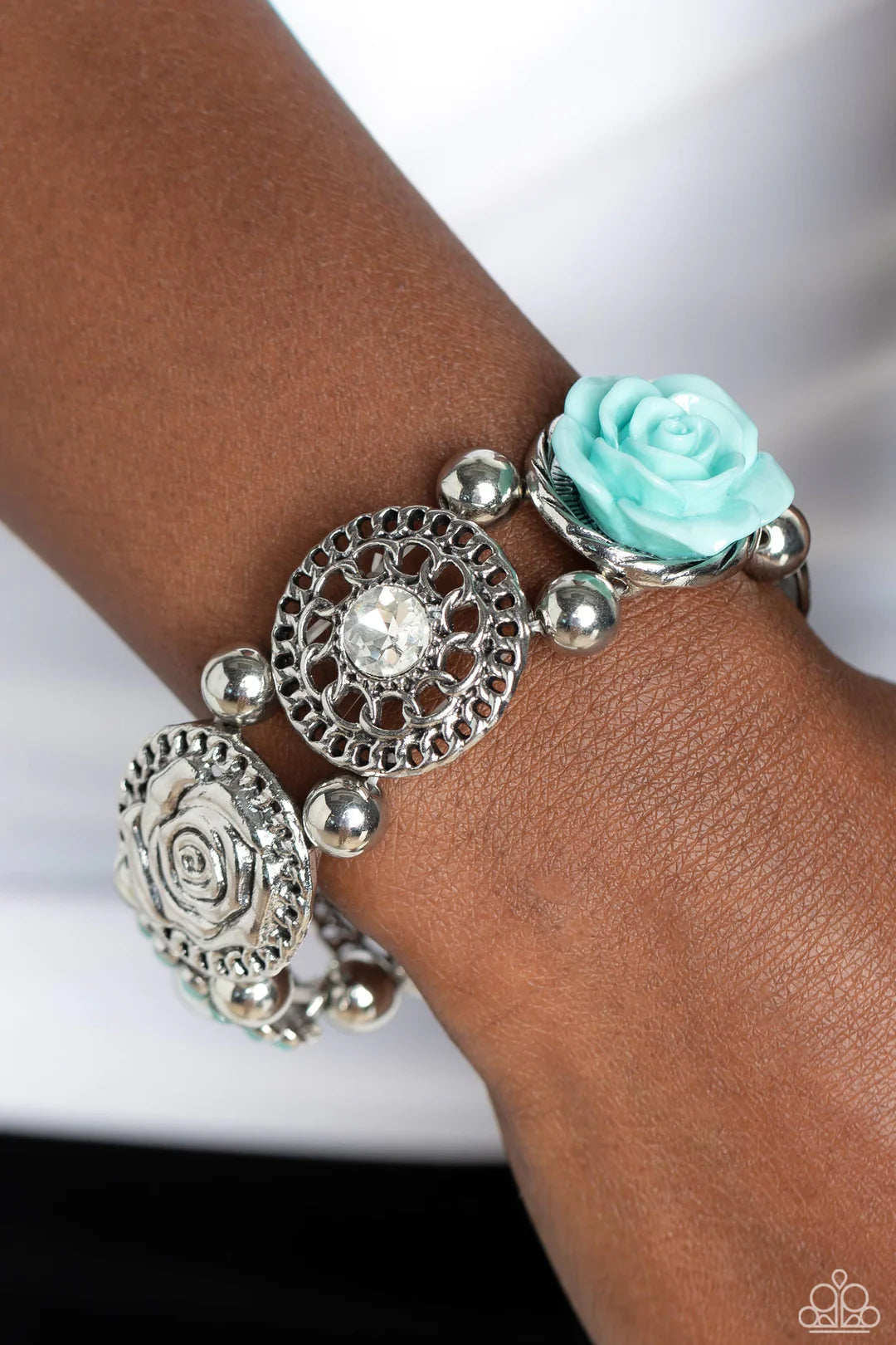 Paparazzi Accessories Optimistic Oasis - Blue Whimsically woven around the wrist on elastic stretchy bands, a Spun Sugar resin rose, a silver disc stamped with a paisley motif, an oversized white gem encased in a textured silver frame, an airy, textured w
