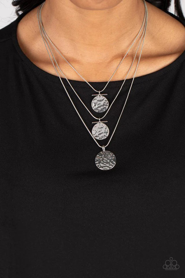 Paparazzi Accessories Dizzying Discs - Silver Three strands of skinny silver snake chain fall into tiered layers as they cascade down the chest. Shiny silver discs hammered in rippling texture slide along each chain in a dizzying display, with thin bars o