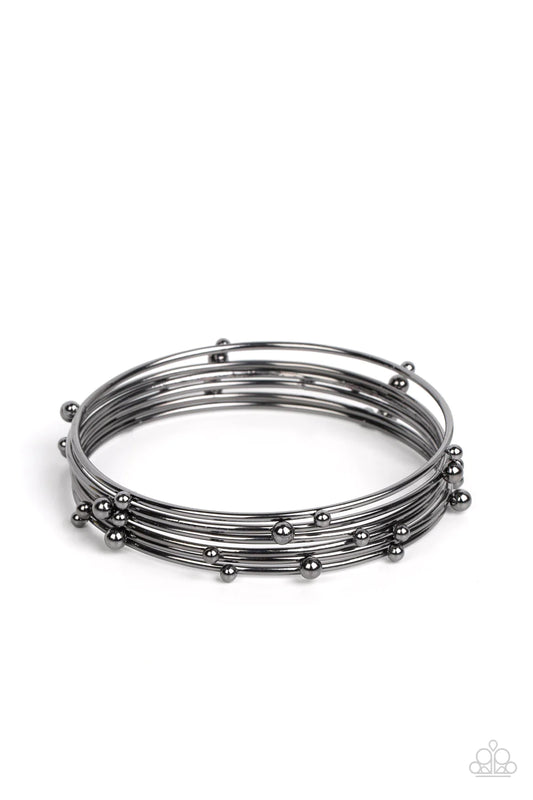 Paparazzi Accessories Metro Satellite - Black Haphazardly dotted with gunmetal studs of varying sizes, a glistening stack of gunmetal bangles glides along the wrist for a noise-making shimmer. Sold as one set of six bracelets. Jewelry