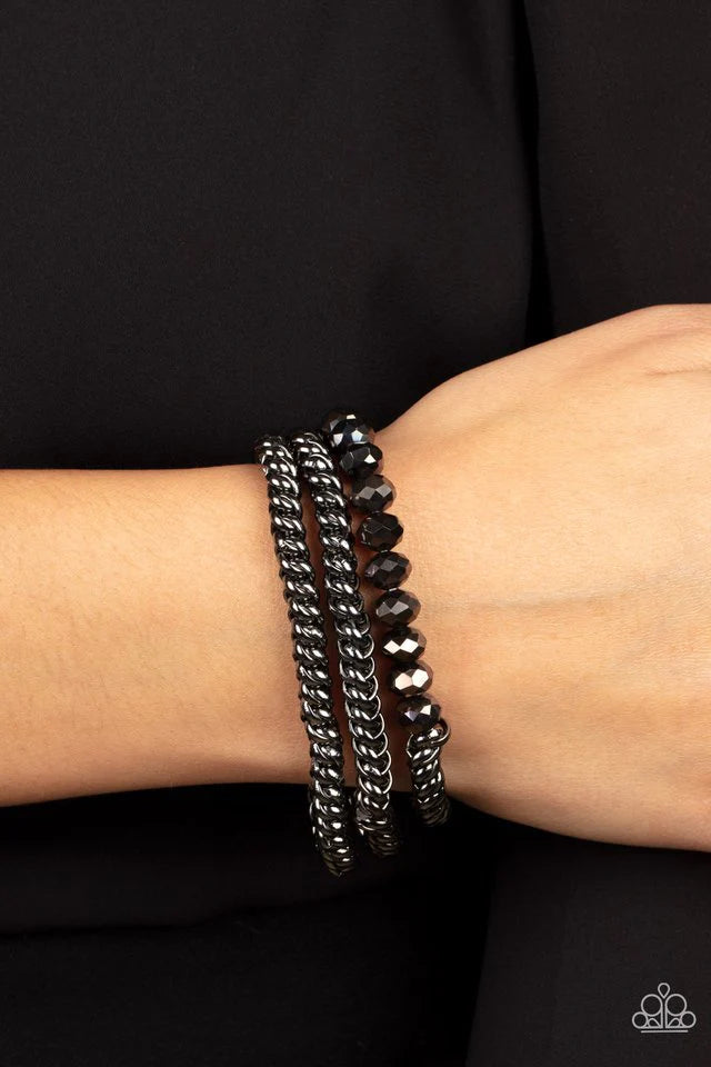 Paparazzi Accessories Gutsy and Glitzy - Black Threaded along stretchy bands, sections of hematite crystal-like beads and interlocking gunmetal chains layer around the wrist for a dash of glitzy grunge. Jewelry