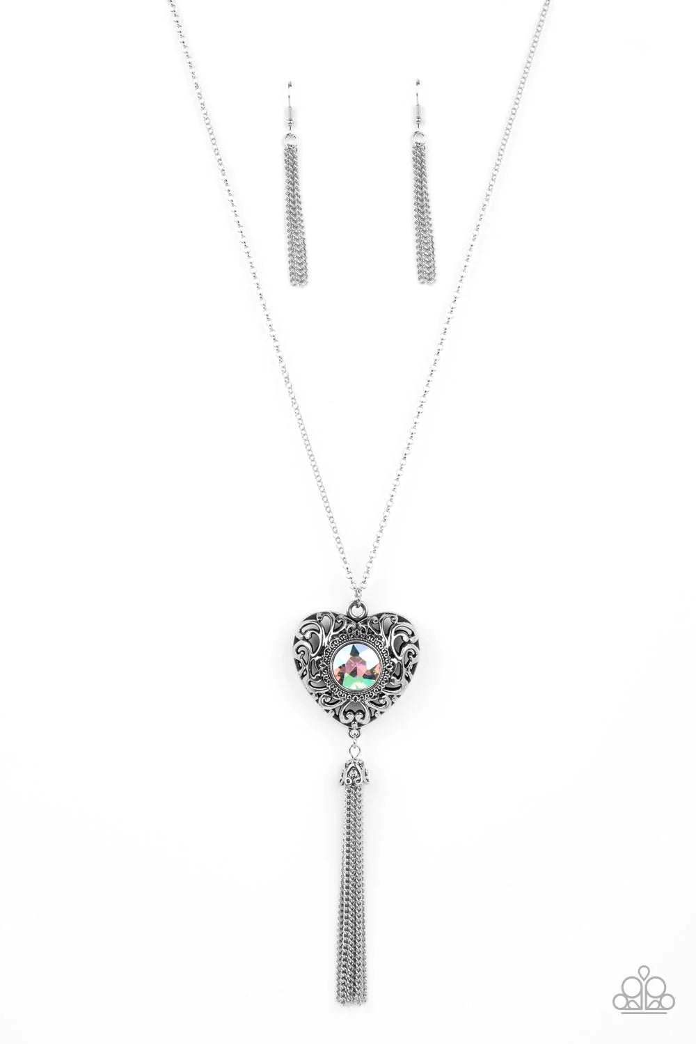 Paparazzi Accessories Prismatic Passion - Green A magical iridescent green gem sparkles at the center of a 3-dimensional silver heart. Filled with vine-like filigree, the locket-inspired heart pendant glides along an extended silver chain while a shimmery