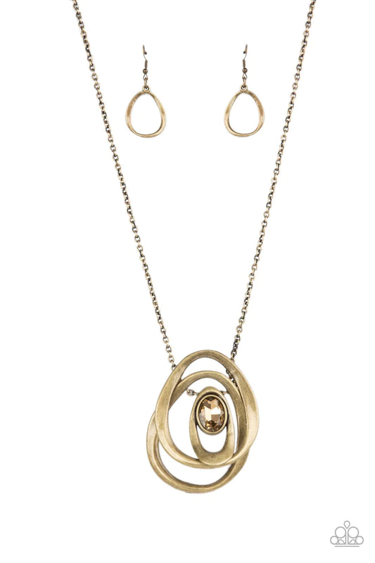 Paparazzi Accessories Luminous Laybrinth - Brass An oversized golden topaz gem seemingly floats inside an asymmetrical brass oval that glides between two oversized brass ovals at the bottom of an extended brass chain, creating an edgy pendant. Features an