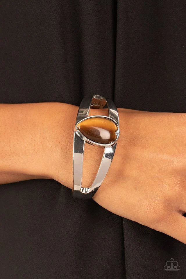 Paparazzi Accessories Enhanced Enchantment - Brown Encased in a sleek silver fitting, an oversized brown cat's eye teardrop stone is pressed into the center of a layered bangle-like bracelet for an enchanting fashion. Features a hinged closure. Sold as on