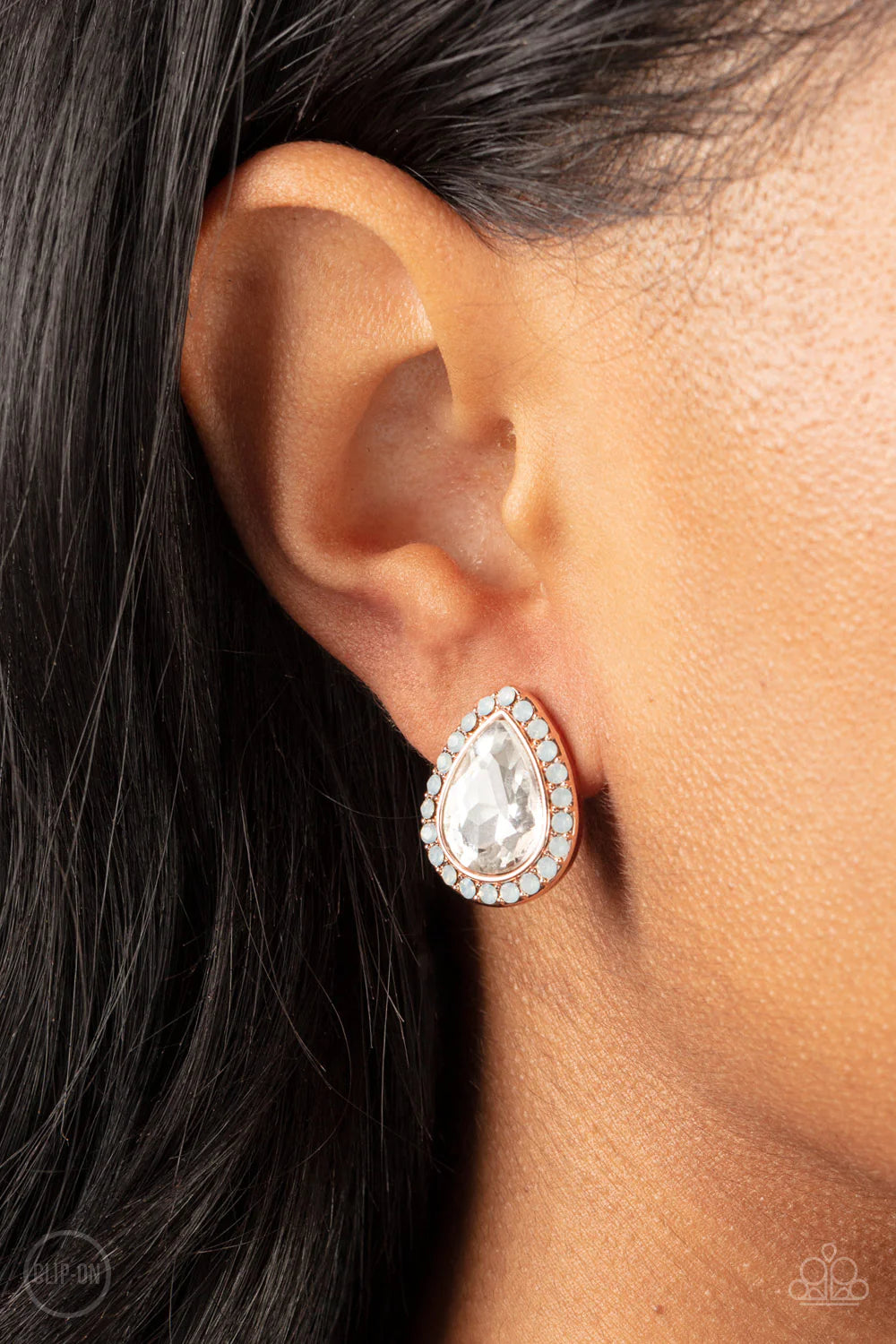 Paparazzi Accessories Cosmic Castles - Rose Gold *Clip-On A faceted white teardrop gem is pressed into a rose gold frame bordered with opalescent white rhinestones for a glamorous finish. Earring attaches to a standard clip-on fitting. Sold as one pair of
