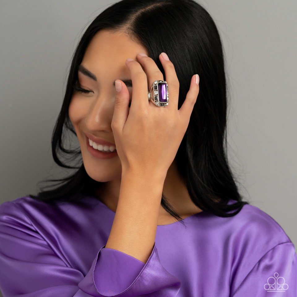 Paparazzi Accessories Radiant Rhinestones - Purple Pressed into a curved, rectangular silver frame, an oversized emerald-cut purple gem shines atop the finger. Dainty square and round gems in shades of white and smoky black airily encircle the oversized g