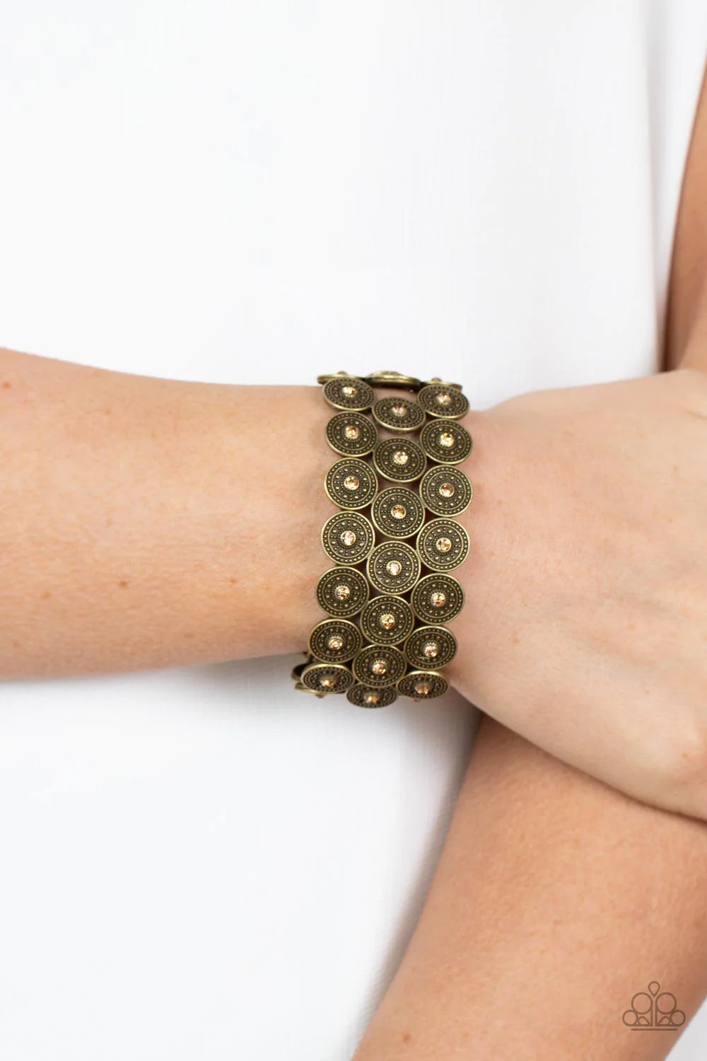 Paparazzi Accessories Forgotten Treasure - Brass Dotted with dainty golden topaz rhinestone centers, studded brass discs haphazardly stack into trios that have been threaded along stretchy bands around the wrist for a whimsical finish. Sold as one individ