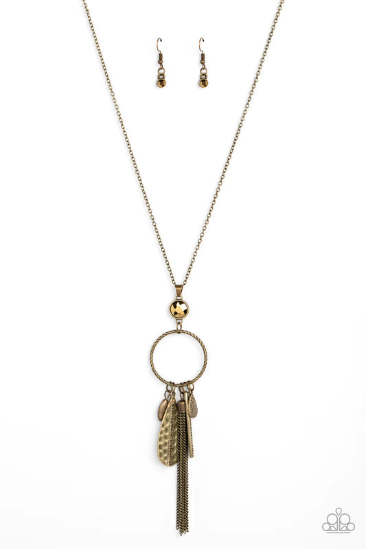 Paparazzi Accessories Tastefully Tasseled - Brass Featuring both smooth and hammered finishes, dainty aurum rhinestones, and a tassel of dainty chains, a sassy collection of brass charms swings from the bottom of a textured circle. A faceted aurum gem sit