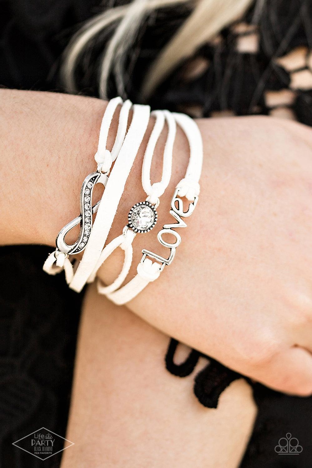 Paparazzi Accessories Infinitely Irresistible - White Strands of white suede knot around silver charms, including a glittery infinity charm, a solitaire rhinestone, and a charm whimsically spelling out “love” across the wrist. Features an adjustable clasp