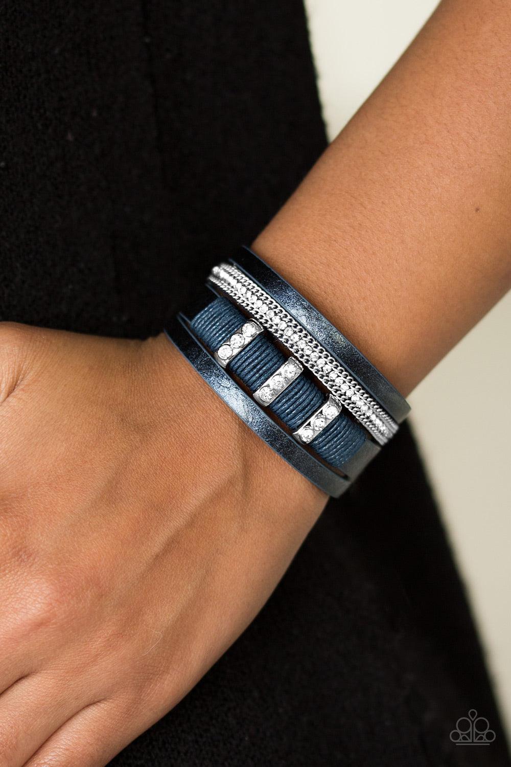 Paparazzi Accessories FAME Night - Blue Metallic blue leather strands layer across the wrist. Infused with silver chain and white rhinestone accents, blue cording knots around a leather strand, securing glittery white rhinestone frames in place for a sass