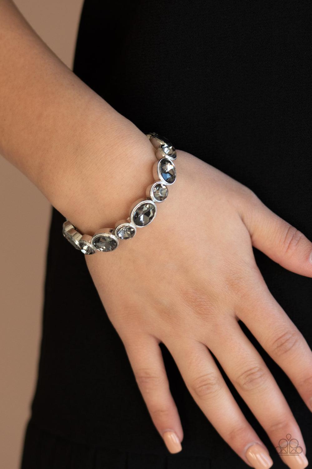 Paparazzi Accessories Still GLOWING Strong - Silver Encased in sleek silver frames, oval and round smoky rhinestones alternate along a stretchy band around the wrist for a timeless look. Sold as one individual bracelet. Get The Complete Look! Necklace: "G