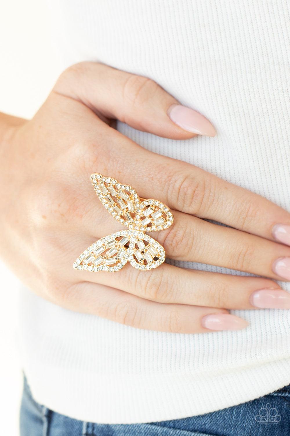 Paparazzi Accessories Flauntable Flutter - Gold Dainty white emerald style rhinestones are sprinkled across the golden wings of a butterfly that is encrusted in glassy white rhinestones for a dramatically dazzling finish. Features a stretchy band for a fl