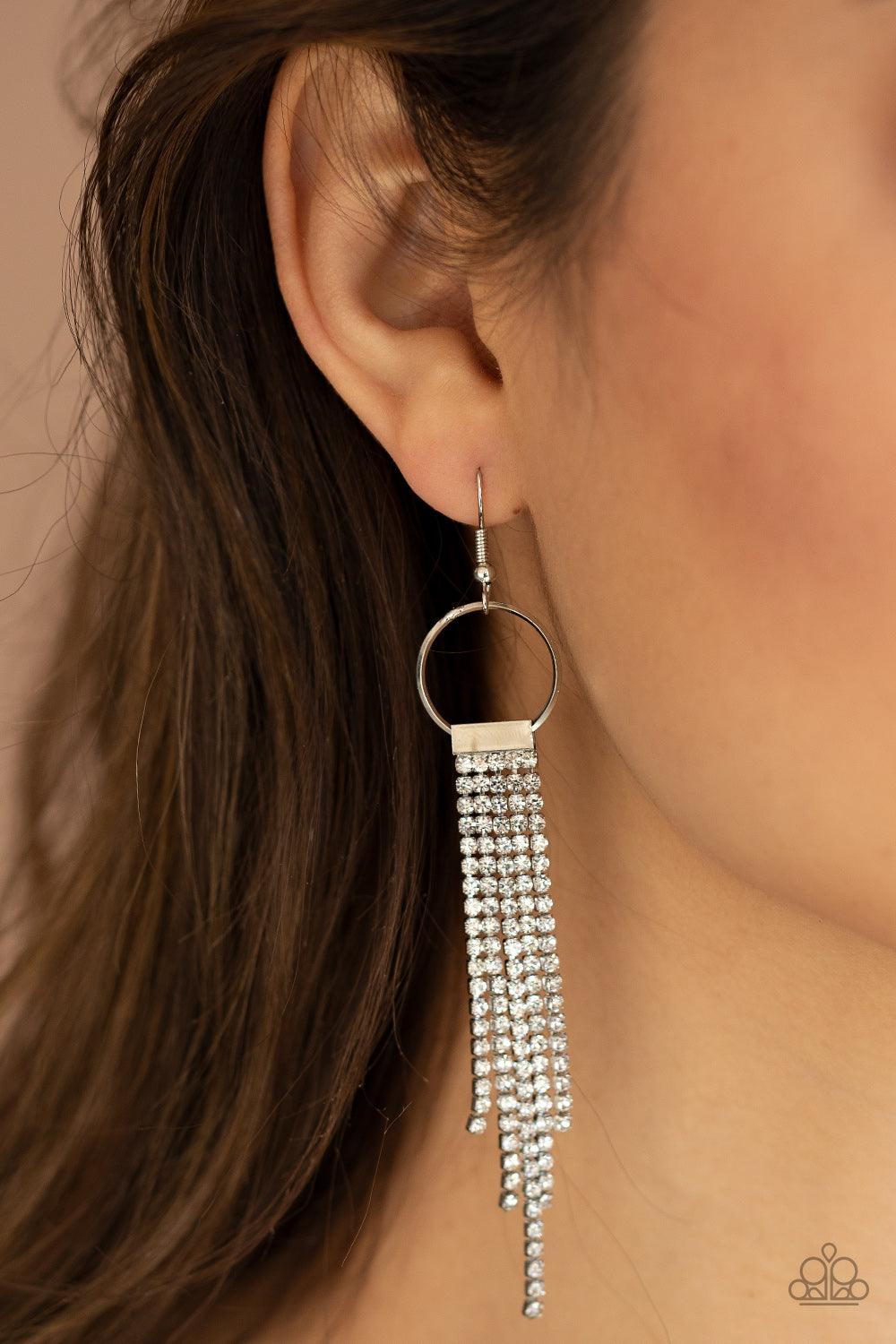 Paparazzi Accessories Tapered Twinkle - White Dainty strands of glittery white rhinestones stream from the bottom of a silver fitting that glides along the bottom of a dainty silver hoop, creating a timelessly tapered fringe. Earring attaches to a standar