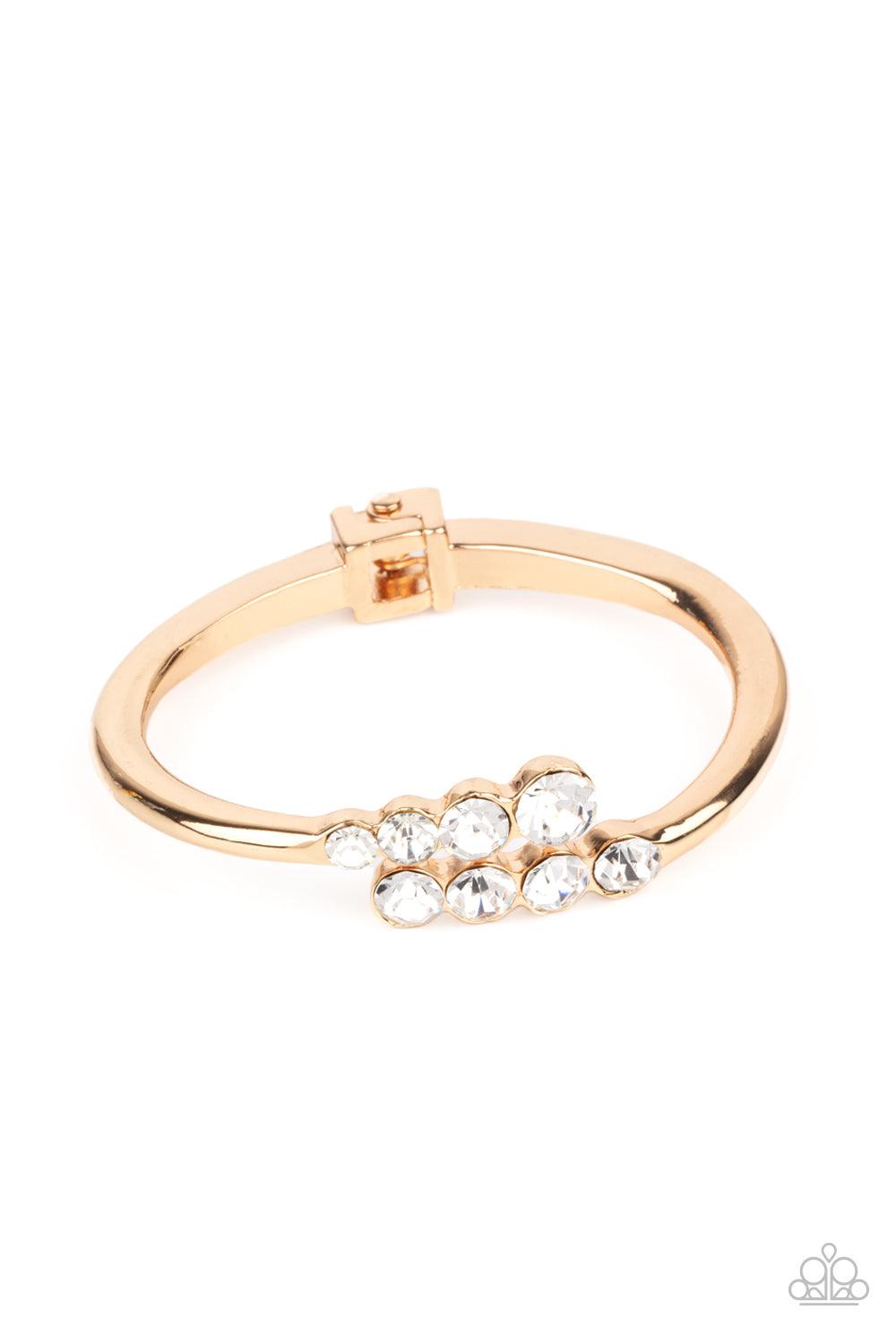 Paparazzi Accessories Defying Dazzle - Gold Attached to two substantial gold bars, oversized rows of glittery white rhinestones delicately stack into a hypnotizing centerpiece around the wrist. Features an adjustable hinge closure. Sold as one individual