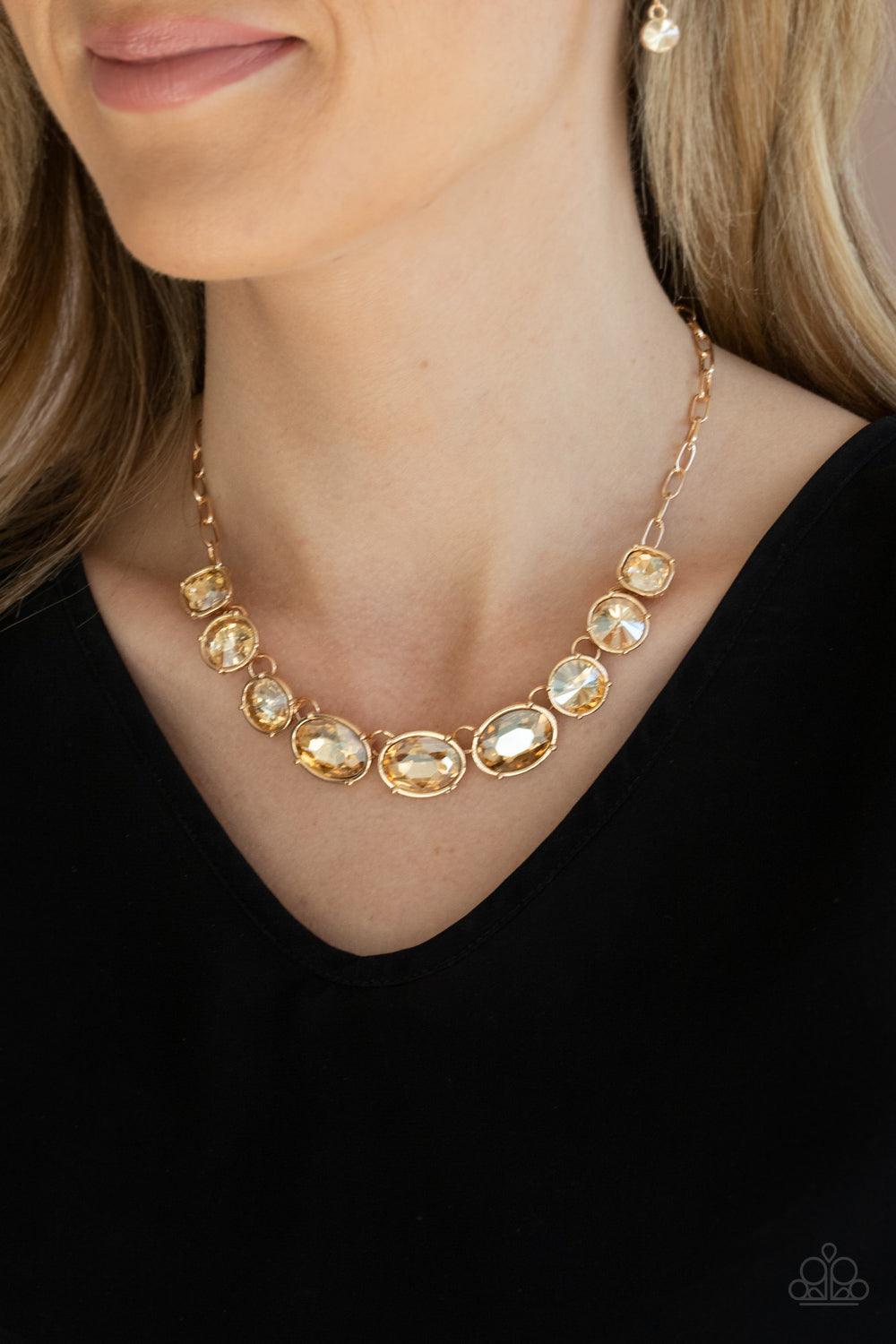 Paparazzi Accessories Gorgeously Glacial - Gold Featuring mismatched round, oval, and square cuts, a golden row of dramatically oversized rhinestones delicately link below the collar for an icy finish. Features an adjustable clasp closure. Sold as one ind