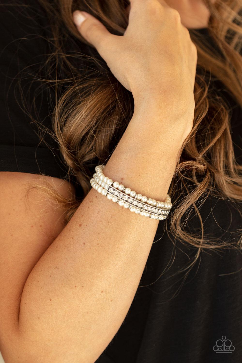Paparazzi Accessories Vintage Beam - White Threaded along stretchy bands, three rows of dainty white pearls are held in place around the wrist by a white rhinestone encrusted centerpiece for a romantic flair. Sold as one individual bracelet. Bracelets