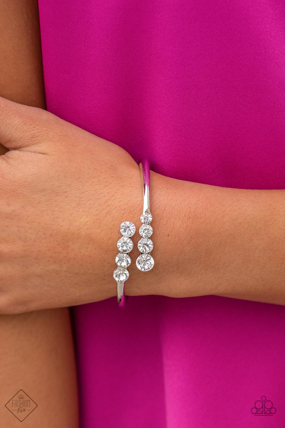 Paparazzi Accessories Defying Dazzle - White Attached to two thick silver bars, oversized rows of glittery white rhinestones delicately stack into a hypnotizing centerpiece around the wrist. Features a hinge closure. Sold as one individual bracelet. Jewel