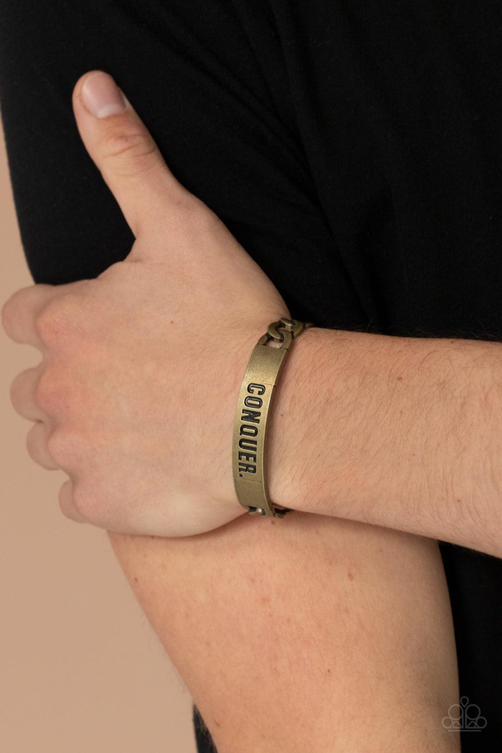 Paparazzi Accessories Conquer Your Fears - Brass Brass chain-like bars attach to a rustic brass centerpiece stamped in the powerful word, "CONQUER," creating a statement-making cuff around the wrist. Sold as one individual bracelet. Jewelry