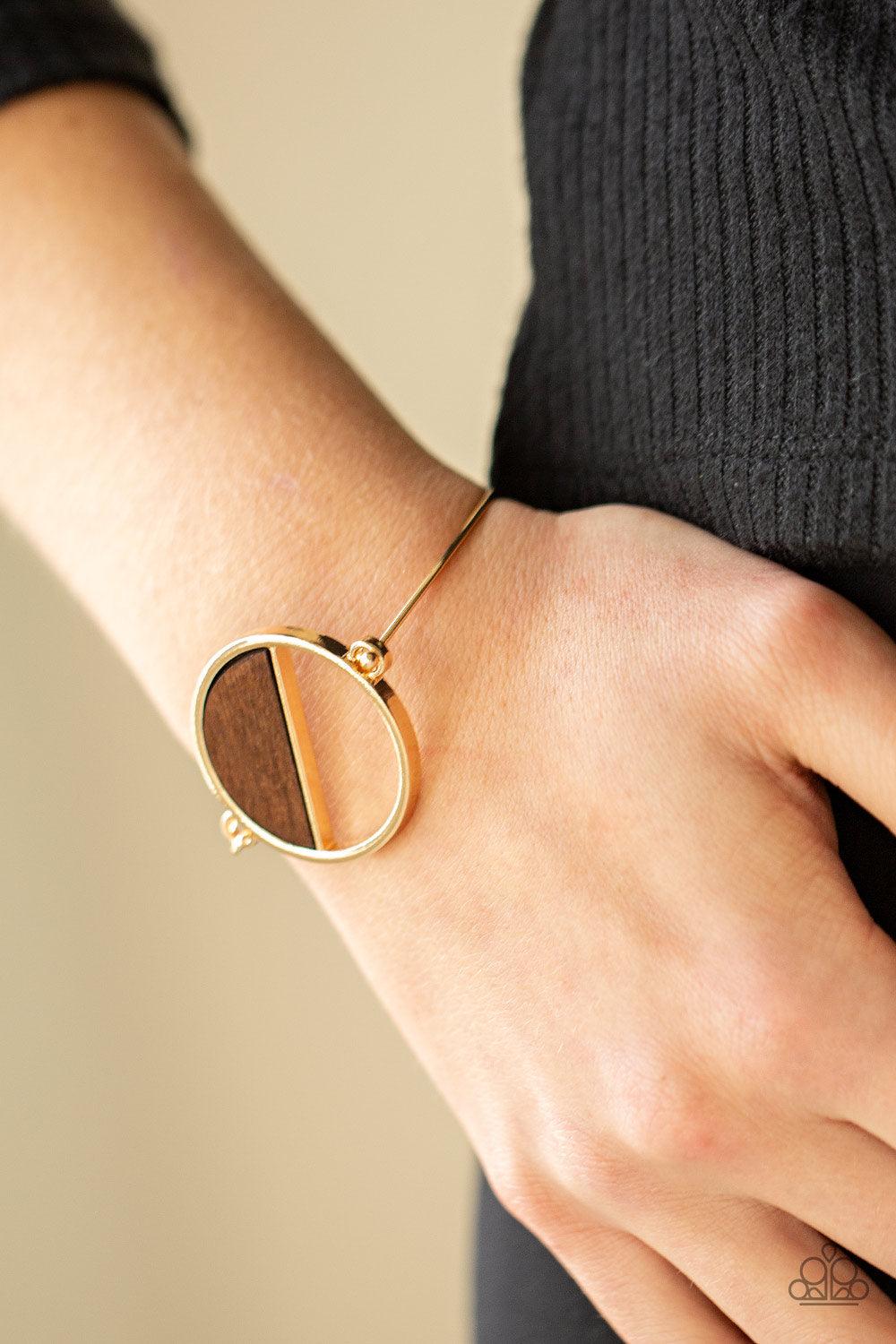 Paparazzi Accessories Timber Trade - Gold Attached to a dainty gold bar that curls around the wrist, a crescent shaped wooden accent adorns half of an airy circular centerpiece for a modern twist. Features a toggle closure. Sold as one individual bracelet