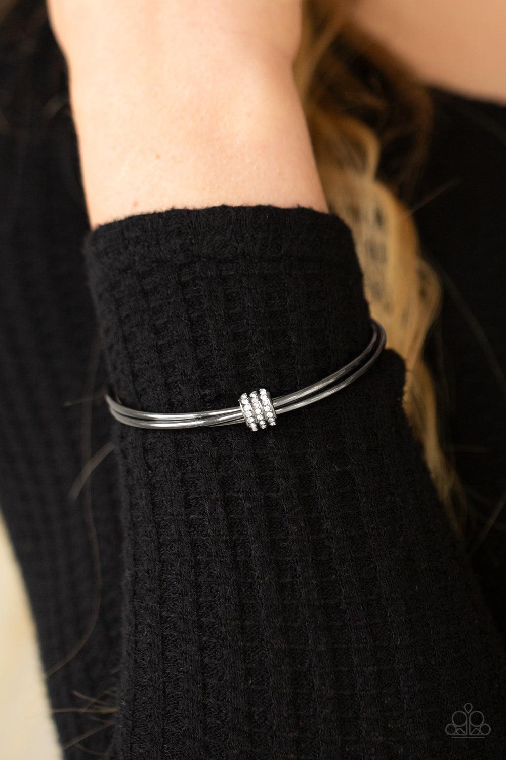 Paparazzi Accessories Roll Out The Rhinestones - Black A white rhinestone encrusted fitting glides along a trio of gunmetal bangles, creating a solitaire bracelet around the wrist. Sold as one individual bracelet. Jewelry