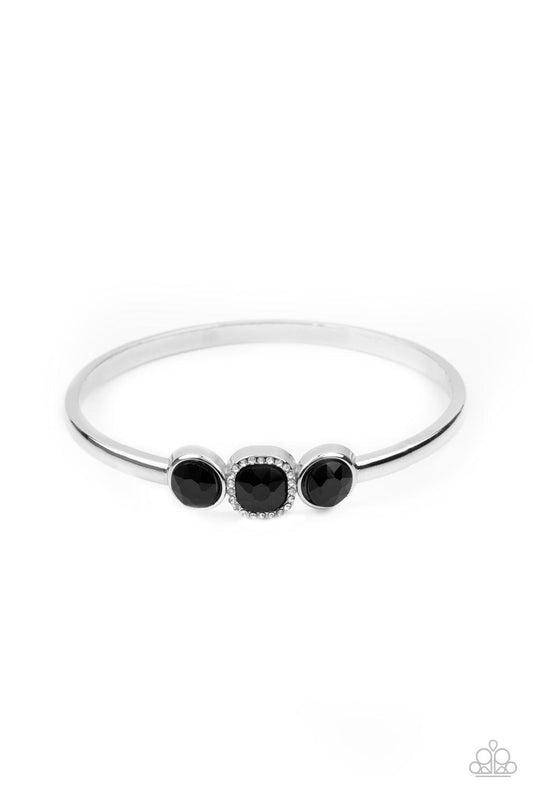 Paparazzi Accessories Royal Demands - Black The center of a thick silver bangle has been adorned with a trio of glittery black rhinestones, creating a sparkly centerpiece around the wrist. Featuring a regal cube cut, the centermost rhinestone is bordered