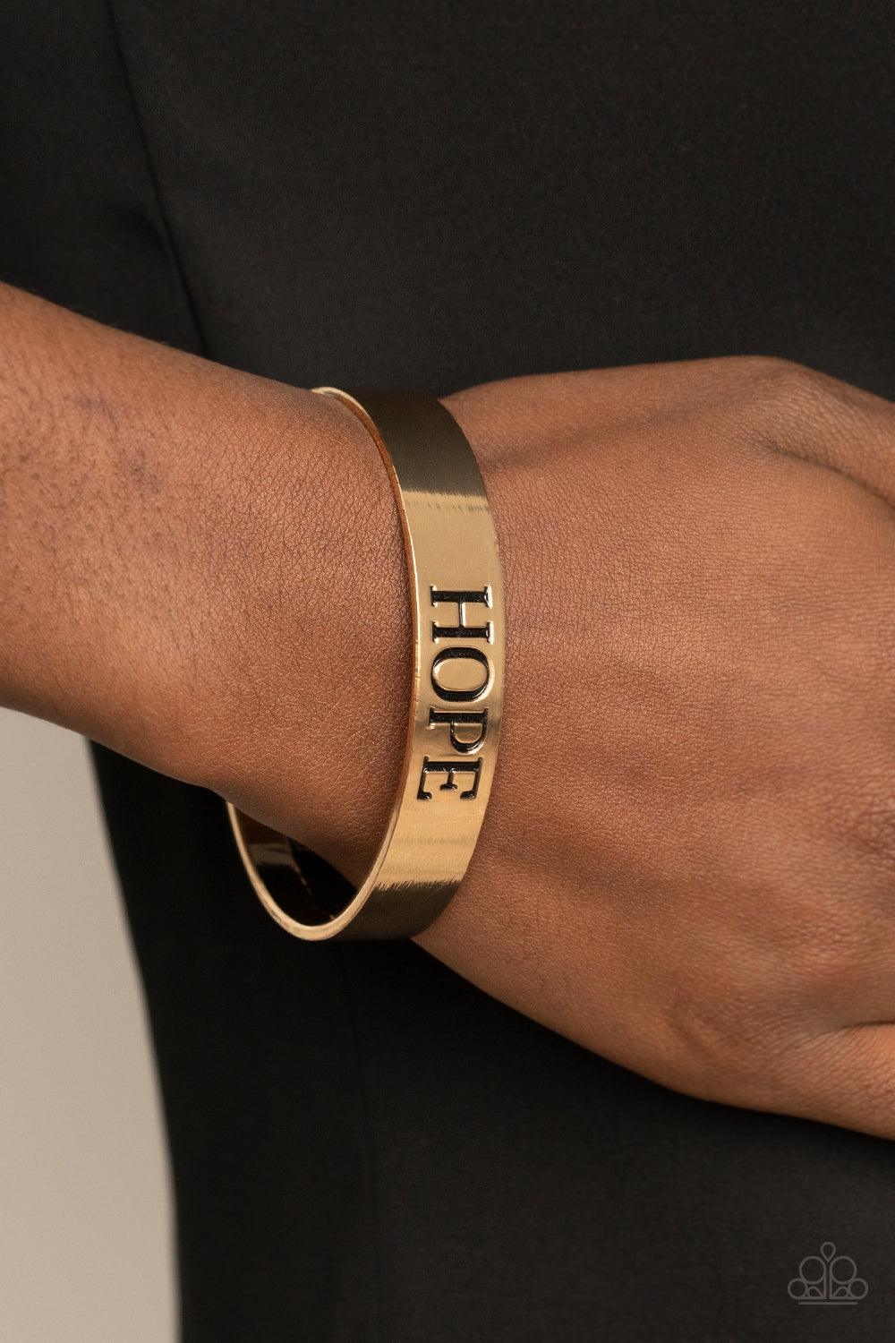 Paparazzi Accessories Hope Makes The World Go Round - Gold The center of a shiny gold cuff is stamped in the word, "Hope," for an inspirational look. Sold as one individual bracelet. Jewelry