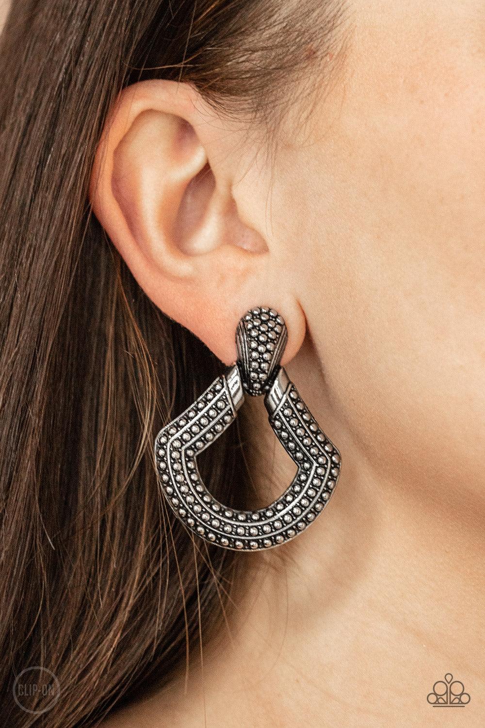 Paparazzi Accessories Better Buckle Up - Silver *Clip-On Dotted in rows of studded details, an oversized silver buckle-like frame adorns the ear for a rustic fashion. Earring attaches to a standard clip-on fitting. Sold as one pair of clip-on earrings. Je