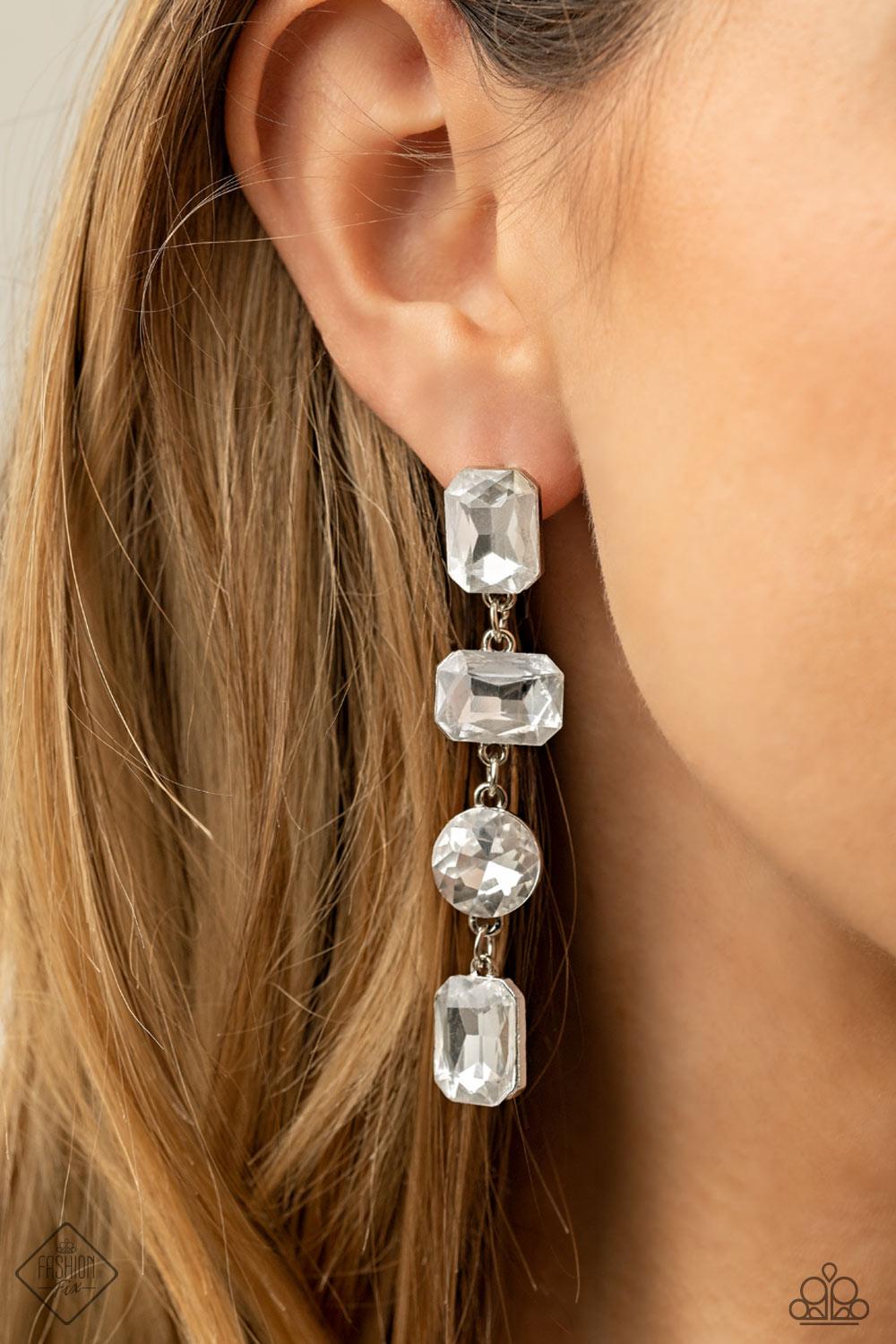 Paparazzi Accessories Cosmic Heiress - White A strand of oversized round, teardrop, and emerald cut rhinestones trickles from the ear, creating a jaw-dropping chandelier. Earring attaches to a standard post earring. Sold as one pair of post earrings. Jewe